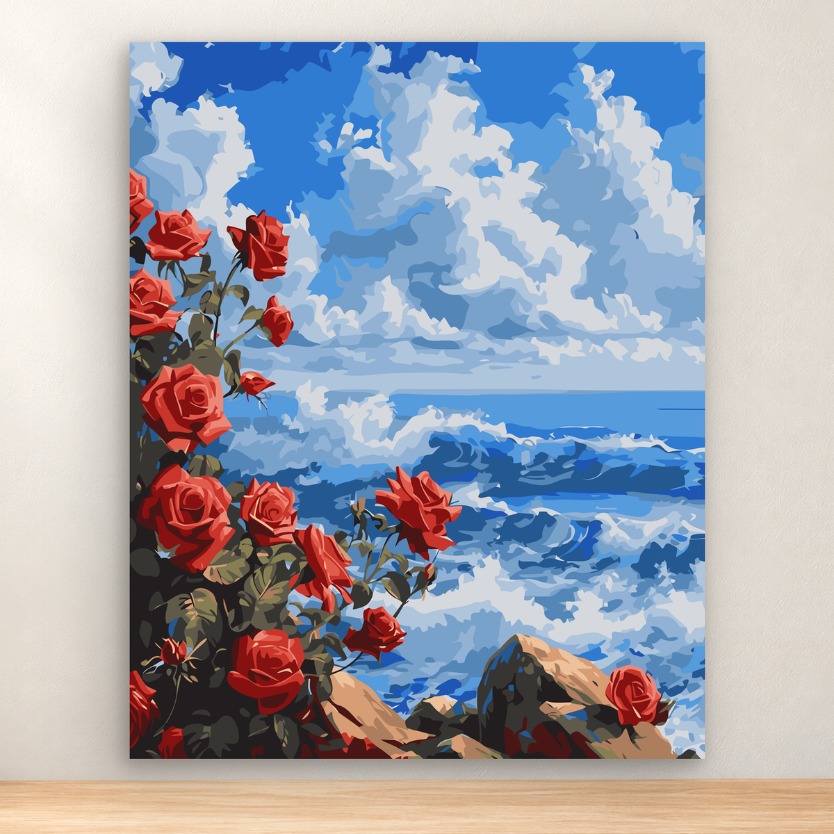 Red roses and dark green foliage beside a blue ocean and rocky coast under layered clouds, 40x50 cm.